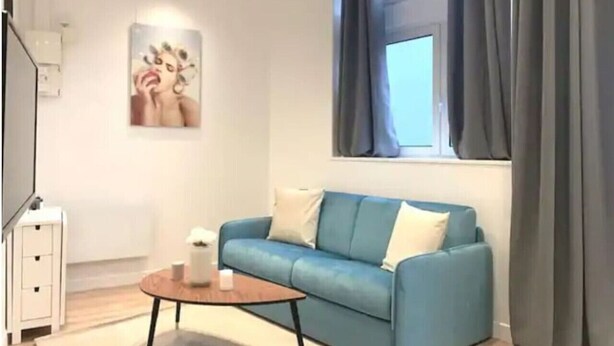 Un salon moderne avec un canapé bleu, une petite table ronde et une fenêtre avec des rideaux.