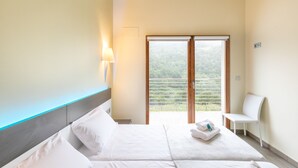 Una habitación de hotel con cama, una silla y balcón con vista a zonas verdes.