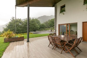 Une terrasse couverte avec une table et des chaises en bois, une vue sur un paysage verdoyant et luxuriant, et un pilier en pierre.