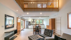 Una sala moderna con sofá, reposapiés y televisor de pantalla plana. Hay una zona de cocina con mesa y sillas.