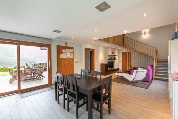 A modern interior with a dining area, kitchen, and living space, featuring wooden floors, a staircase, and a sliding glass door to a patio.