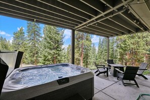 A hot tub with a view of a forest, outdoor seating, and a pergola structure.