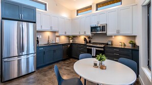 Una cocina moderna con armarios blancos, un refrigerador de acero inoxidable, un microondas y un comedor con una mesa redonda y sillas.