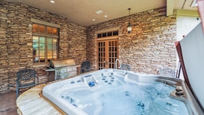 A stone-walled room with a hot tub, a grill, and a window with glass doors. - 8,000+ Sq Ft Breck Ski Home, Hot Tub, Theater, Pool Table, Sleeps 14 (Breckenridge)