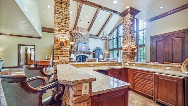 A spacious kitchen with a stone accent wall, wooden cabinets, and a large island with a sink. - 8,000+ Sq Ft Breck Ski Home, Hot Tub, Theater, Pool Table, Sleeps 14 (Breckenridge)