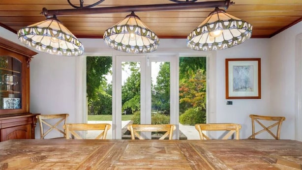 A dining area with a wooden table and chairs, a stained glass ceiling, and a view of a garden through glass doors.