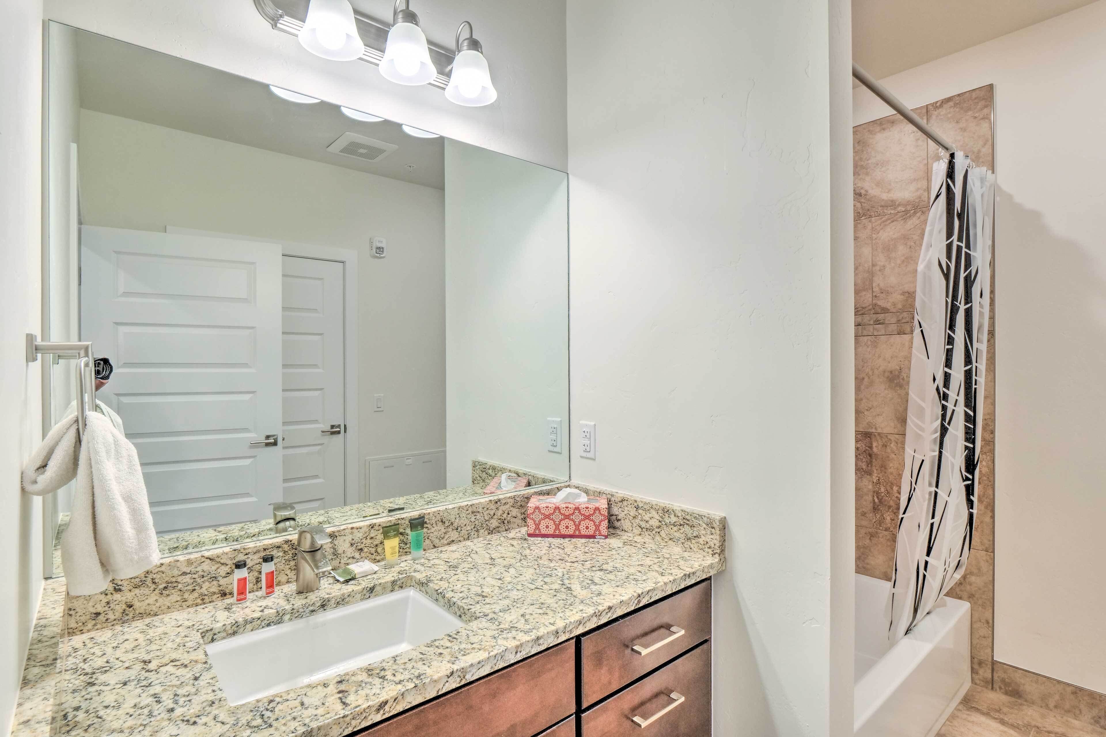 A bathroom with a granite countertop, a white sink, a large mirror, and a shower curtain with a black and white pattern.