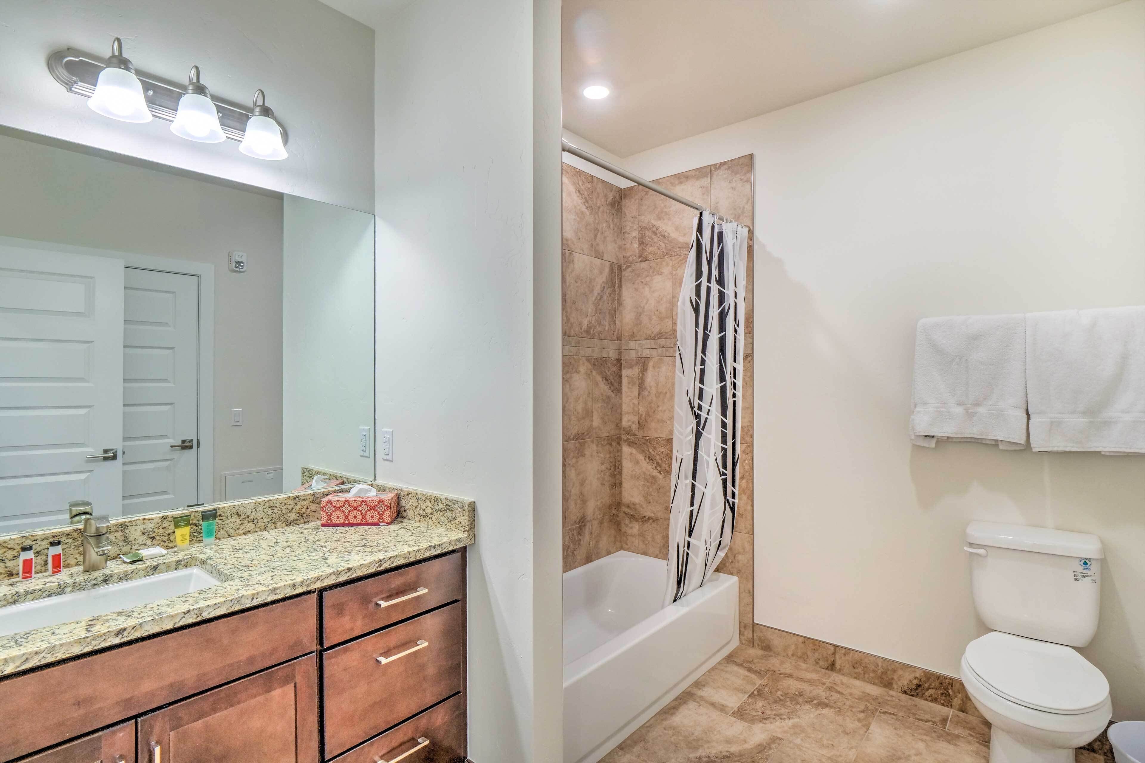 A bathroom with a granite countertop sink, a mirror, a shower with a black and white shower curtain, and a white toilet.
