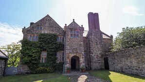 A historic stone building with a prominent tower, a large arched entrance, and a well-maintained lawn. - Y Fferm (Mold)