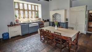 A kitchen with a large island, wooden chairs, and a window with bars. - Y Fferm (Mold)