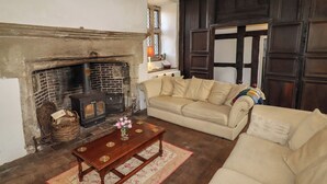 A cozy living room with a fireplace, a beige sofa, a wooden coffee table, and a patterned rug. - Y Fferm (Mold)