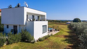 Una casa moderna de dos pisos con balcón, piscina y un jardín bien cuidado.