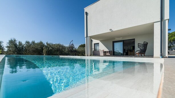 Una casa moderna con piscina, mobiliario exterior y una vista despejada del cielo.