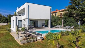 Una casa moderna de dos pisos con piscina, mobiliario exterior y un jardín bien cuidado.