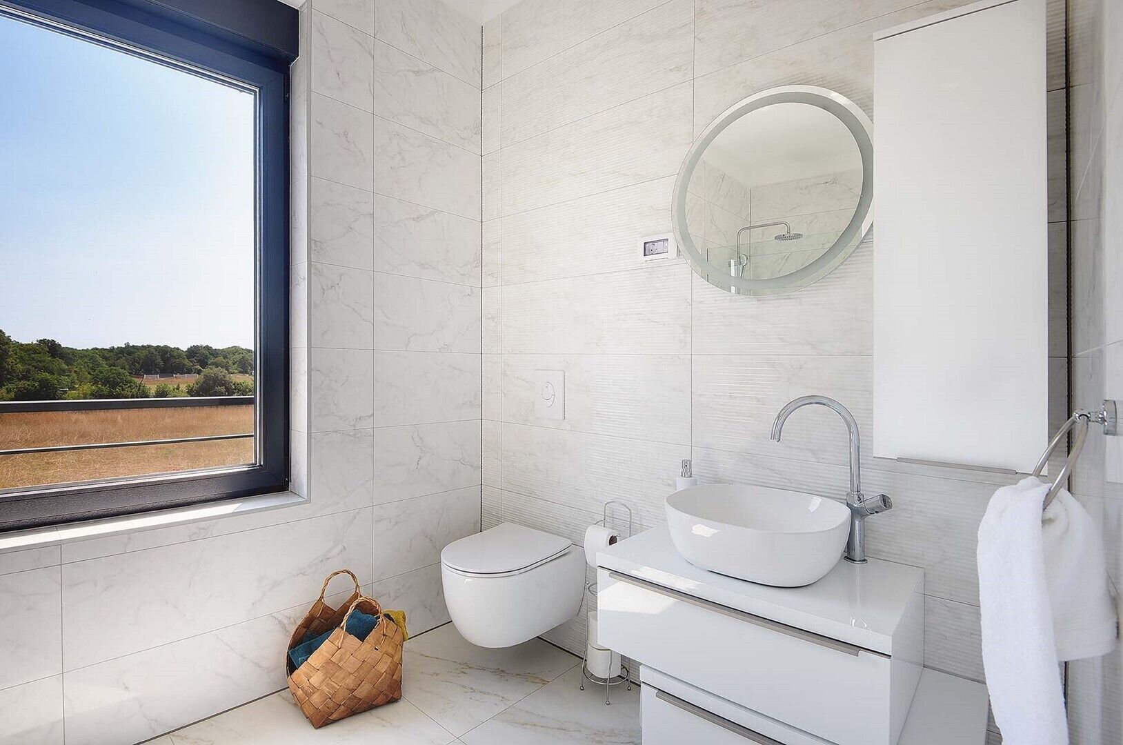Baño con inodoro, bidé, lavamanos y un ventanal grande.