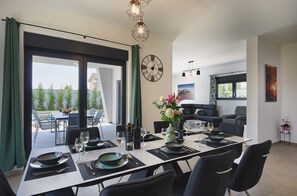Un coin repas avec une table dressée pour six personnes, un canapé et une horloge au mur.