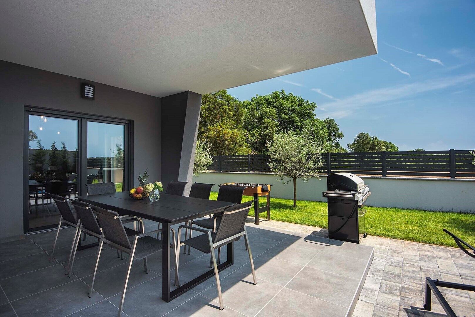 An outdoor patio with a dining table and chairs, a grill, and a view of the surrounding area.