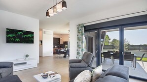 A modern living room with a flat-screen TV, grey sofas, a coffee table, and a dining area with a table and chairs. - Villa Tika in Jadreski (Jadreski)