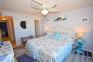 A bedroom with a bed, a ceiling fan, a round mirror, and wall art.