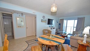A living room with a round wooden table, a sofa, a TV, and a window with curtains. - Marigot Beach 303 2 Bedroom Condo by RedAwning (Ocean City)