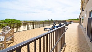 A wooden deck with lounge chairs and a small table, overlooking a beach and a fence. - Marigot Beach 303 2 Bedroom Condo by RedAwning (Ocean City)