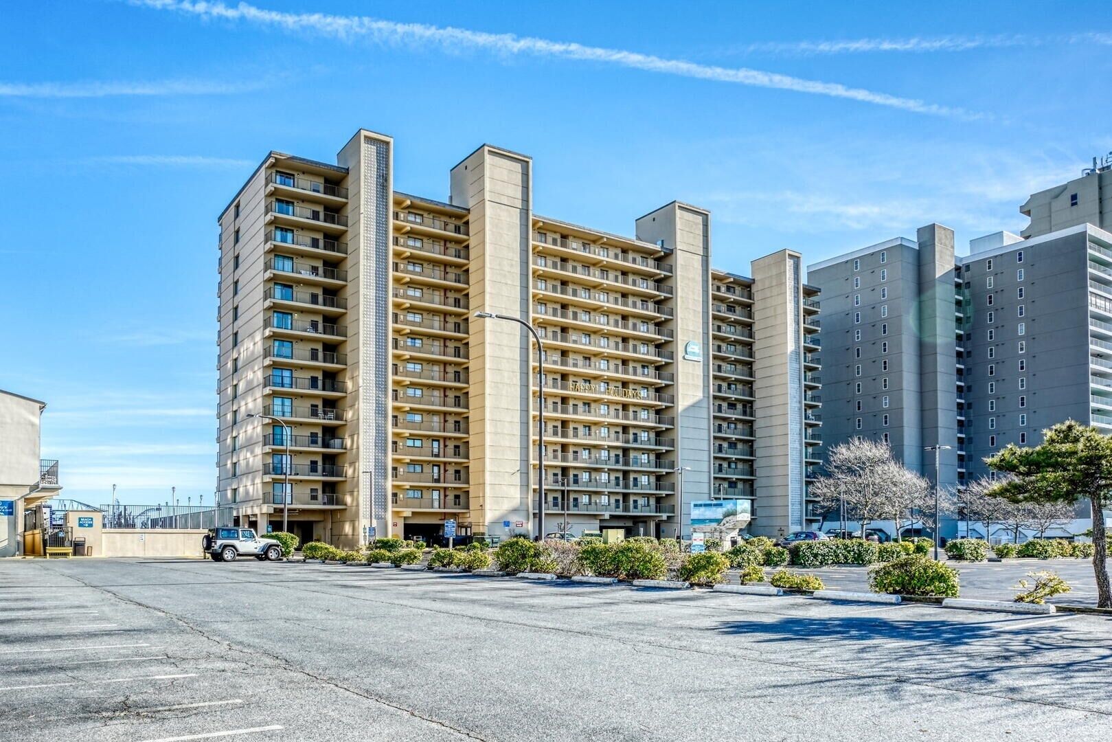 A multi-story hotel with a central courtyard, featuring a parking lot and a clear blue sky.