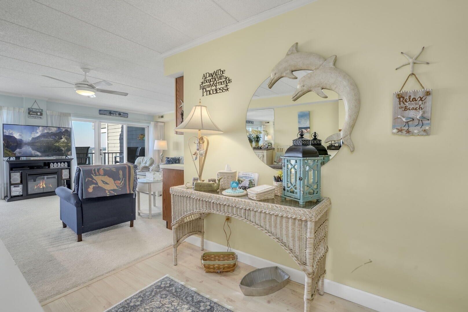 A living room with a fireplace, a television, a sofa, a console table with decorative items, and a wall with a mirror and dolphin artwork.