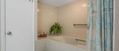 Une salle de bain comprenant une baignoire, un espace douche, un porte-serviettes et une porte dotée d’une poignée décorative.