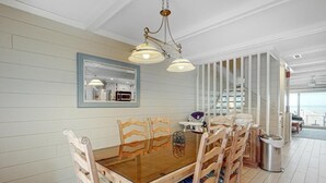 A dining area with a wooden table and chairs, a chandelier, and a staircase leading to an upper level. - Pilot House 5 4 Bedroom Townhouse by RedAwning (Ocean City)