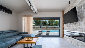 A modern living room with a sofa, a coffee table, and a TV mounted on a stone wall. - Villa Neven with heated private pool,wine cellar (Seoca)