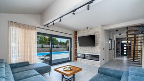 A modern living room with a stone fireplace, a flat-screen TV, and a pool view. - Villa Neven with heated private pool,wine cellar (Seoca)