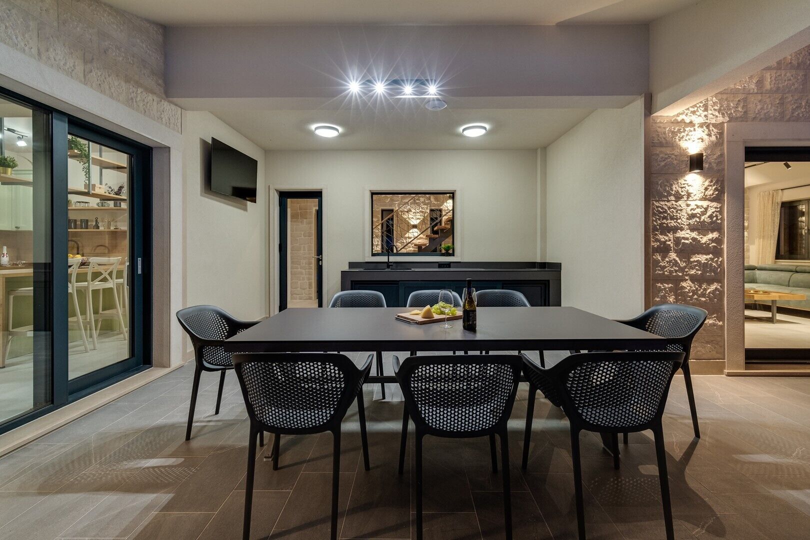 Un espace repas moderne avec une table rectangulaire, six chaises noires et une cloison en verre d’un côté.