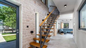 A modern interior with a spiral staircase against a stone wall, leading to a living area with a sofa and a coffee table. - Villa Neven with heated private pool,wine cellar (Seoca)