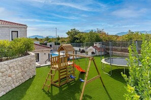 Quintal com balanço de madeira, trampolim e uma piscina pequena.