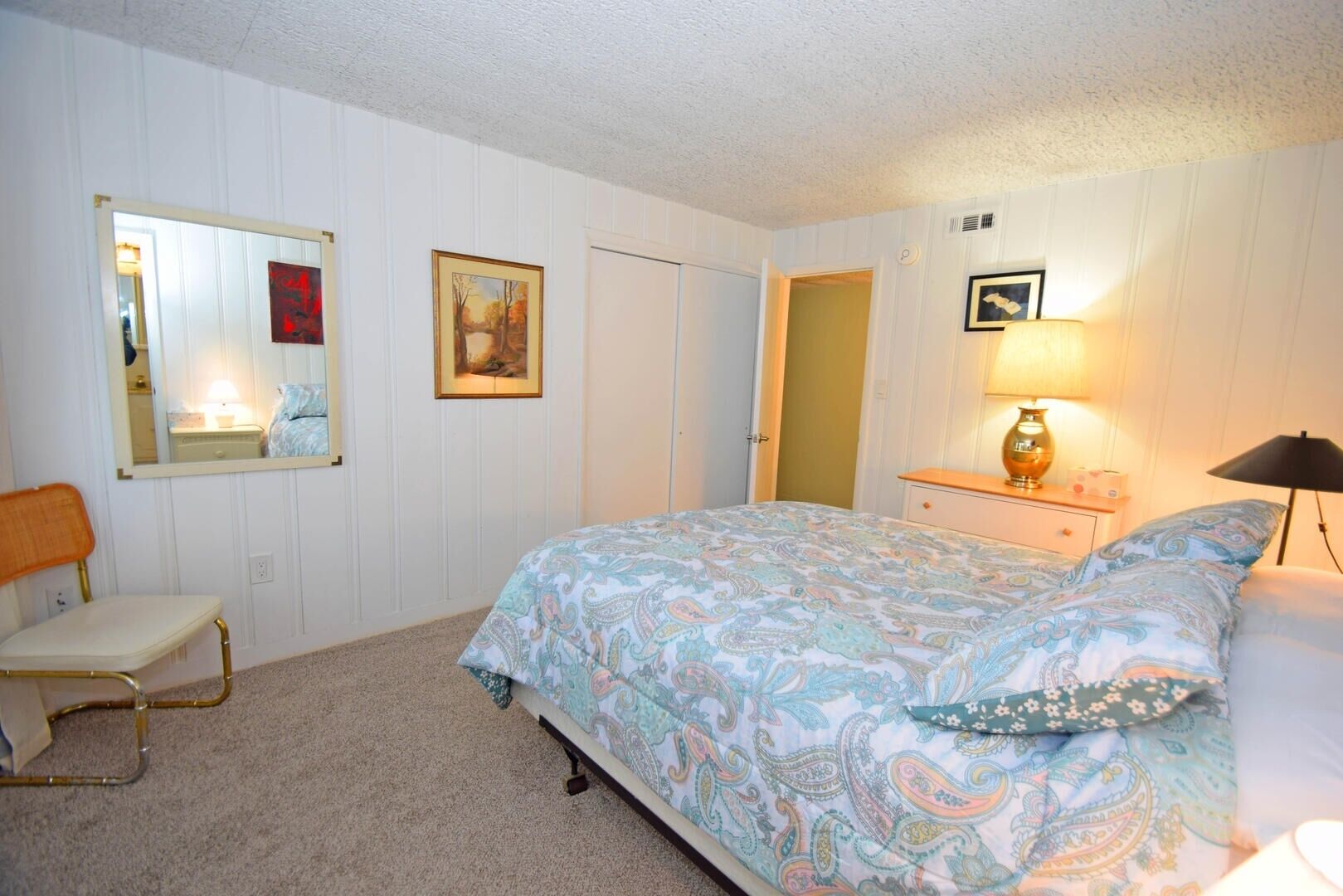 A bedroom with a bed, a chair, a dresser, a mirror, and a door.