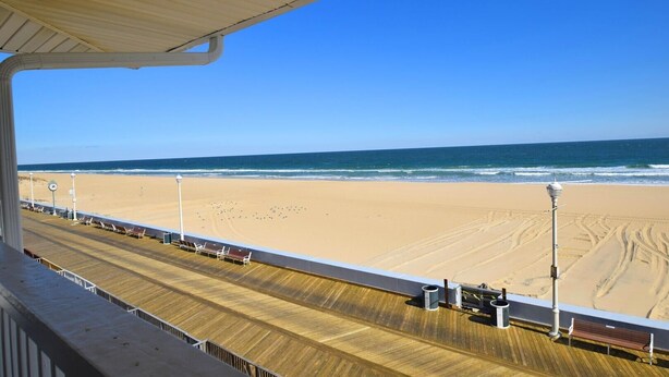 A wooden deck with a view of a sandy beach and ocean under a clear blue sky.