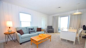 A living room with a sofa, a coffee table, a lamp, a chair, a dining table, and curtains.