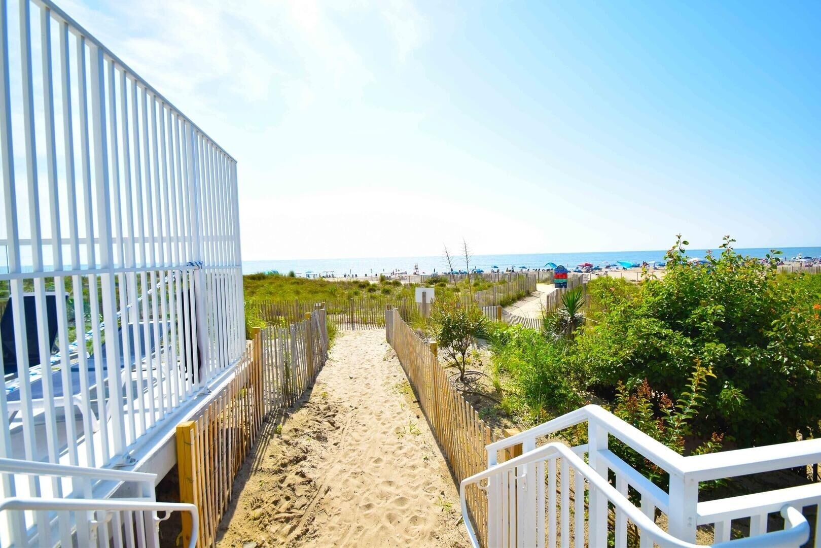 A sandy pathway leading to a beach with a wooden fence and white railings.