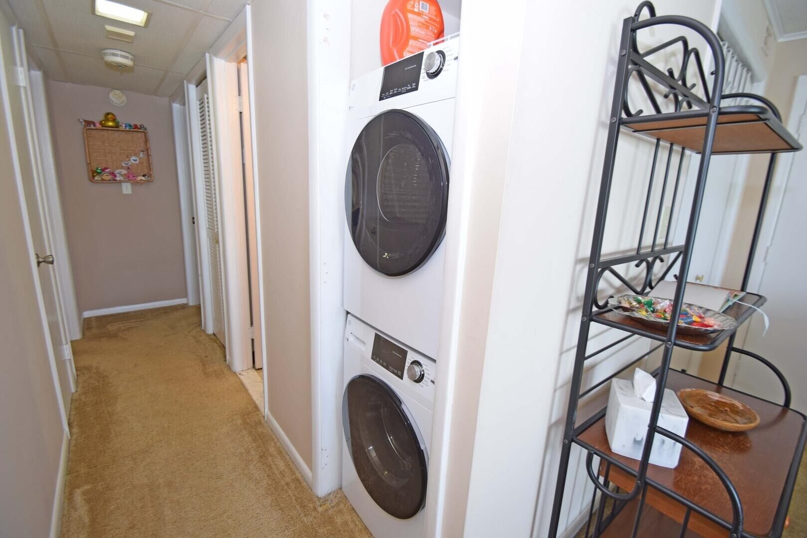 A laundry room with two stacked front-loading washing machines and a metal drying rack with various items.