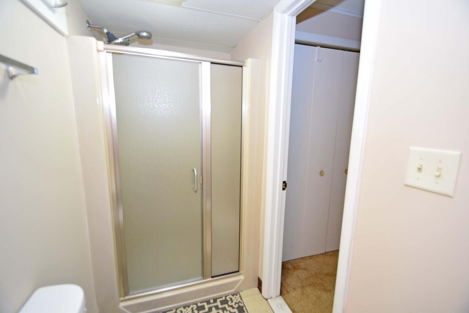 Une salle de bain avec douche, toilettes et une porte donnant sur une autre pièce.