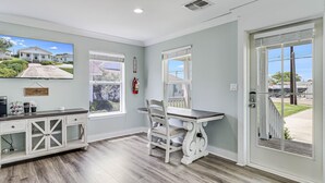 A room with a wooden floor, a white desk with a chair, a television mounted on the wall, and a window with blinds. - Coast Oaks Cottage 5 1 Bedroom Cottage by RedAwning (Rockport)