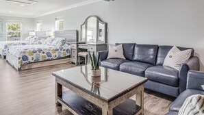 A modern bedroom with a bed, bedside tables, a dresser, a mirror, and a seating area with a couch and coffee table. - Coast Oaks Cottage 5 1 Bedroom Cottage by RedAwning (Rockport)