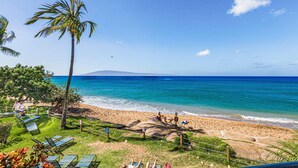 A beach with lounge chairs, a palm tree, and a view of the ocean. - Sands Of Kahana 315 2bd/2ba Oceanfront 2 Bedroom Condo by RedAwning (Lahaina)