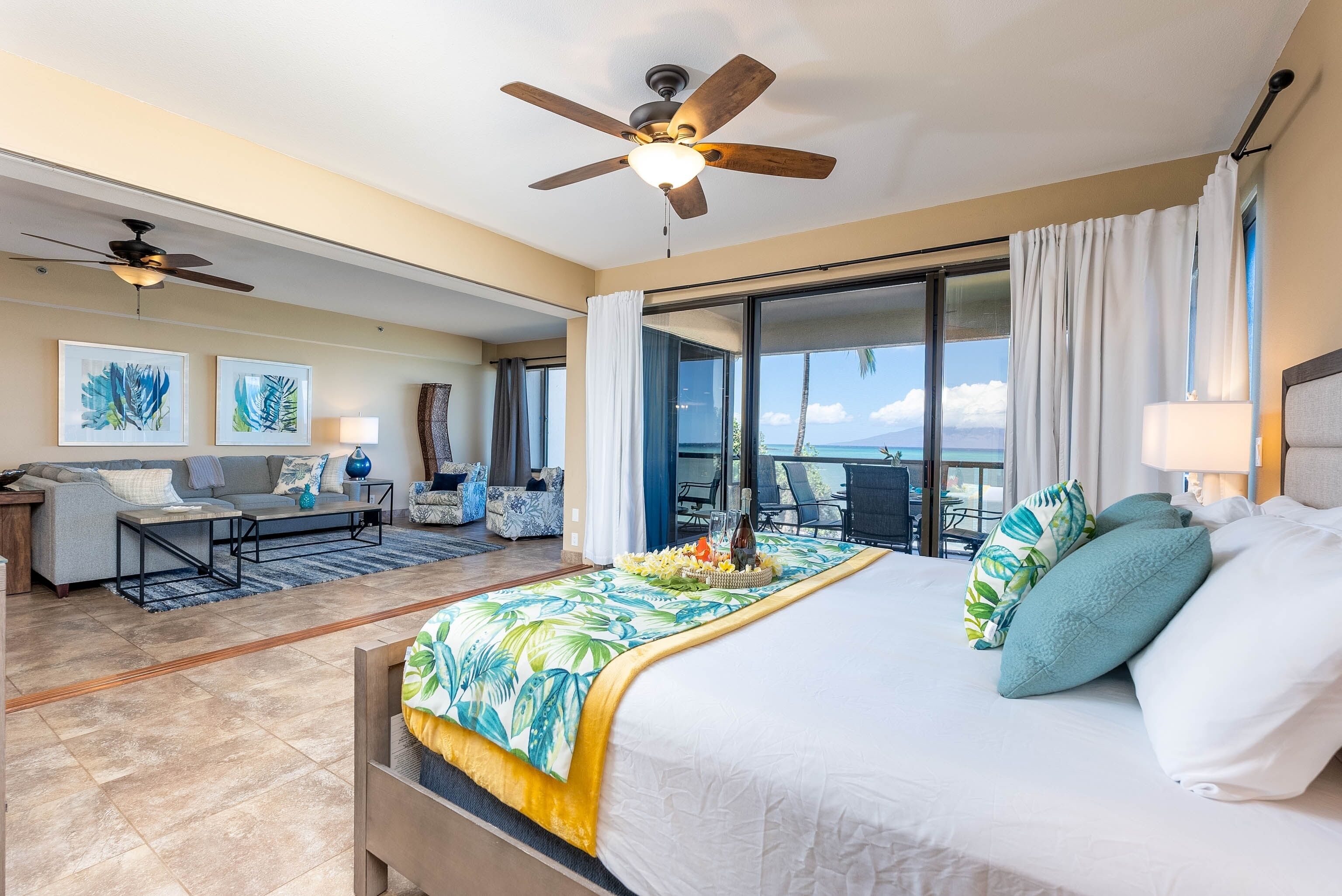 Quarto de hotel com uma cama grande, ventoinha no teto, sofá, mesa de jantar e varanda com vista.