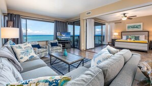 A spacious living room with a large sofa, a coffee table, and a TV. There is a balcony with a view of the ocean. - Sands Of Kahana 315 2bd/2ba Oceanfront 2 Bedroom Condo by RedAwning (Lahaina)