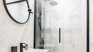 Ein modernes Badezimmer mit einer gläsernen Dusche, einem runden Spiegel und einem dunklen Holzwaschtisch mit weißem Waschbecken.