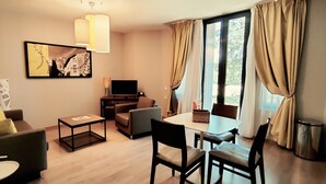 A modern living room with a sofa, coffee table, TV, and dining area. - Le Château des Plans (Parthenay)