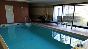 A swimming pool with a slide, a door, and a window with a view of greenery. - Le Château des Plans (Parthenay)