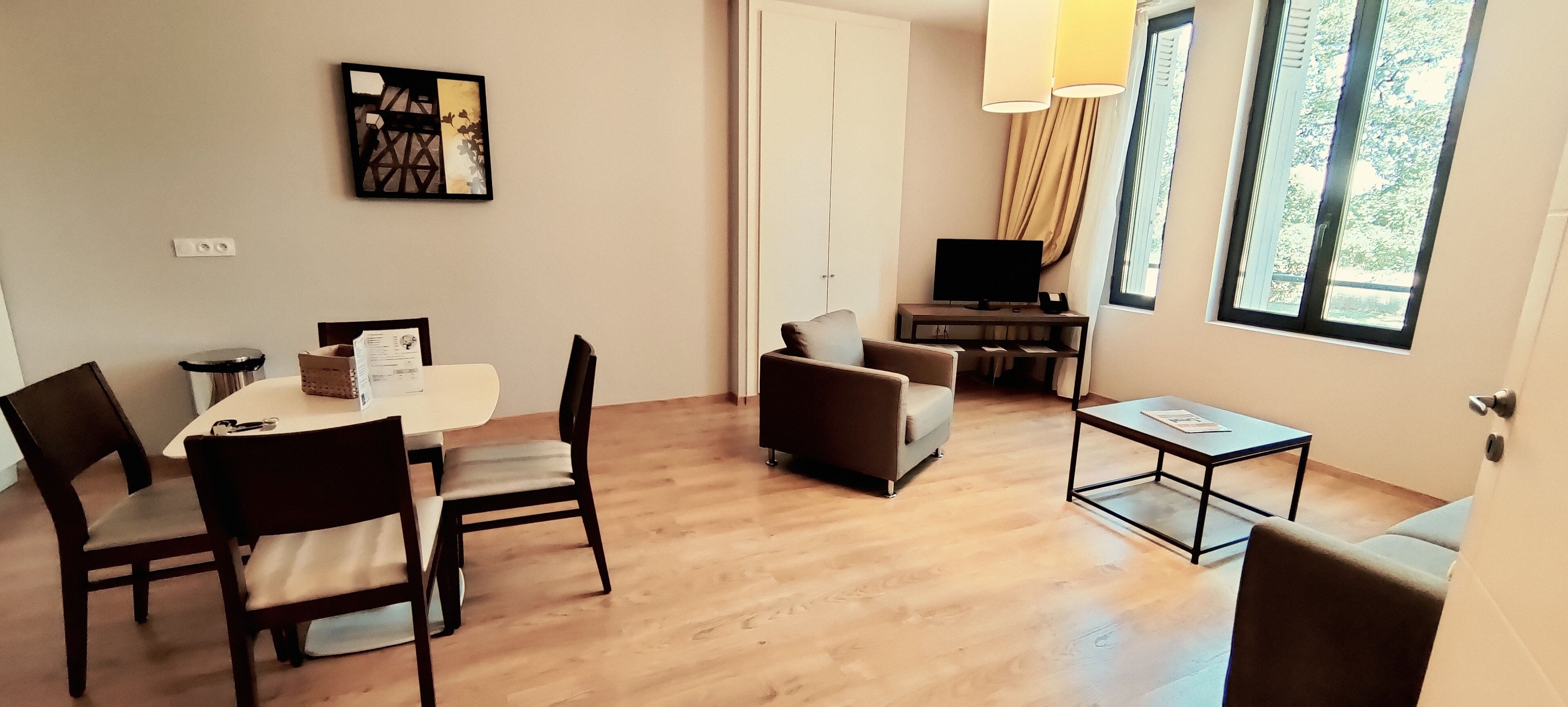 A modern living room with a dining table, chairs, a sofa, a TV, and a window with curtains.