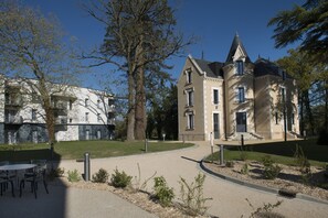 Un edificio grande e histórico con torreta y fachada de piedra, rodeado de un césped cuidado y árboles.